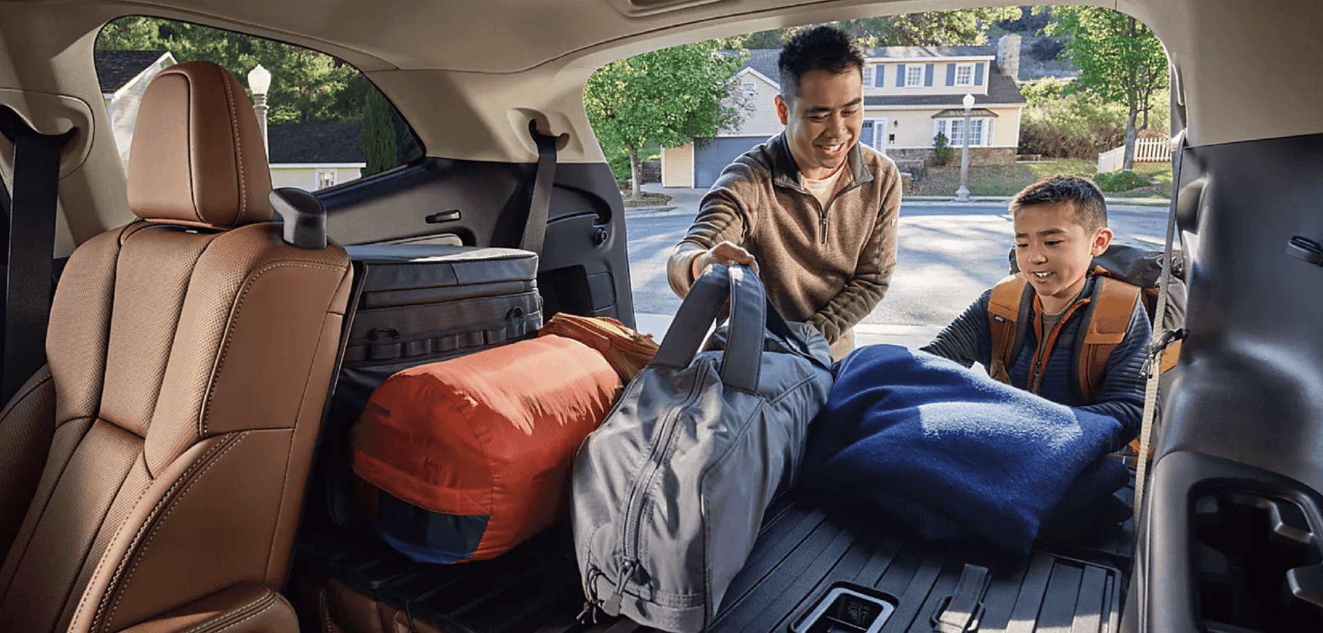 Father and son loading camping gear and duffel bags into the spacious cargo area of a Subaru SUV outside their home.