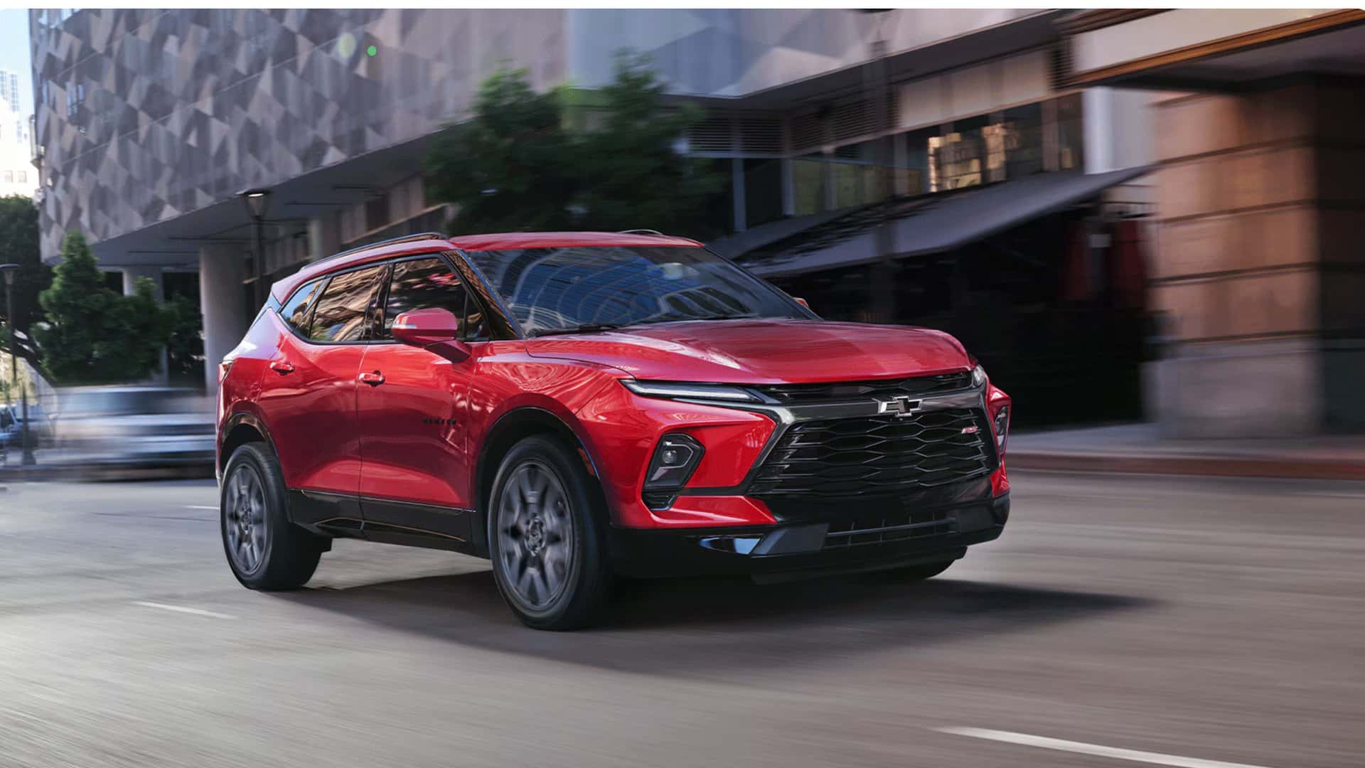 2026 Chevrolet Blazer RS red SUV driving through downtown city streets in front three-quarter view.