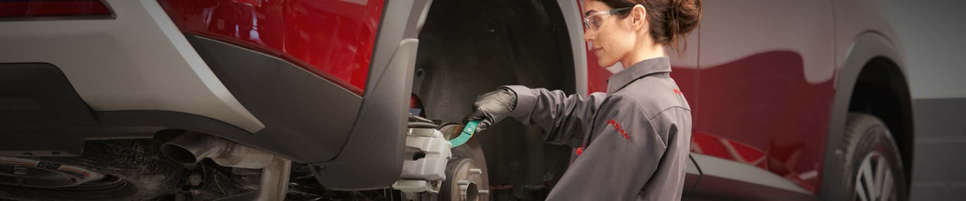 A Nissan Service Technician installs new brake pads on a Nissan car's rotor in a bright, clean service center.