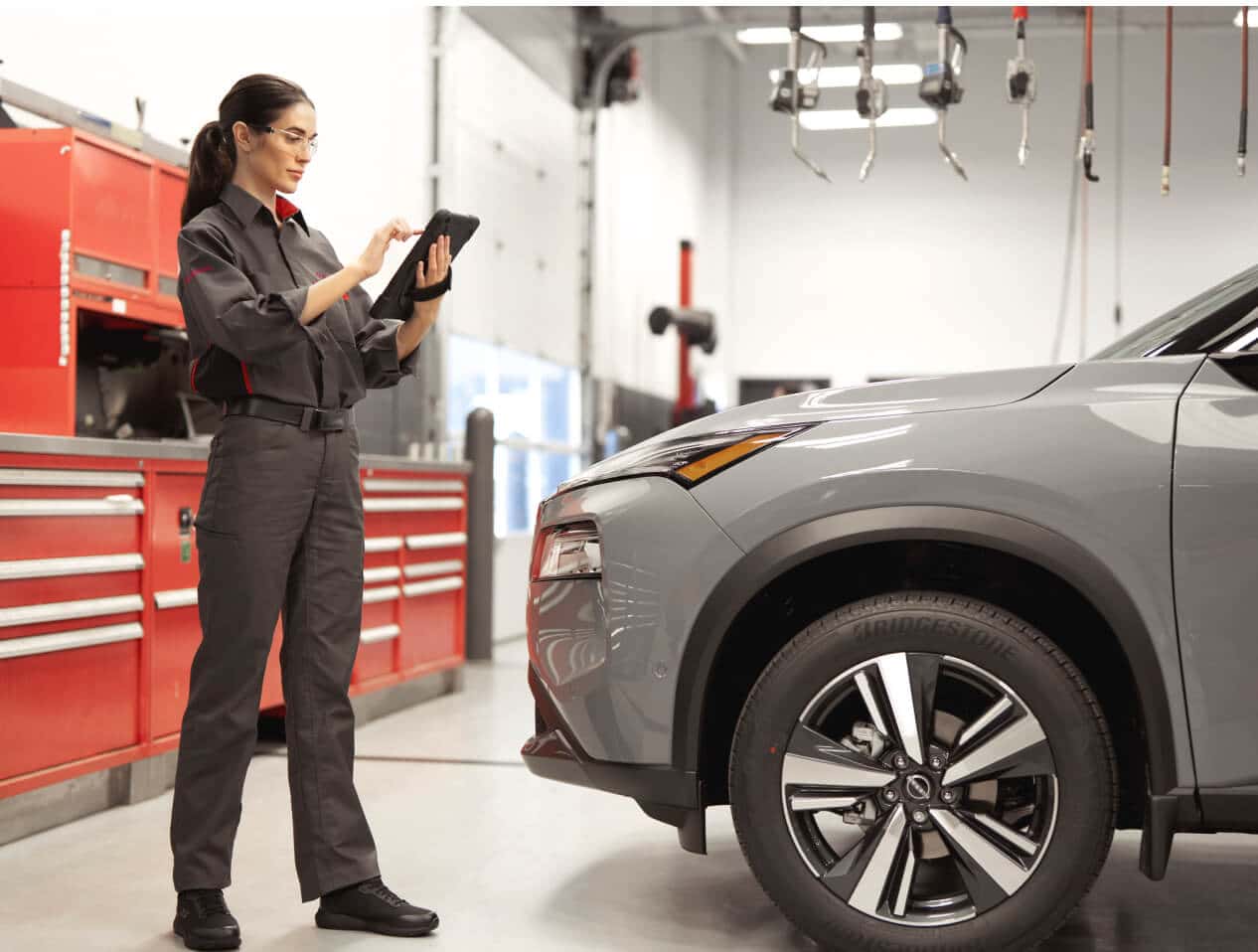 A Nissan Service Technician confidently holds a tablet near a car in a service center.