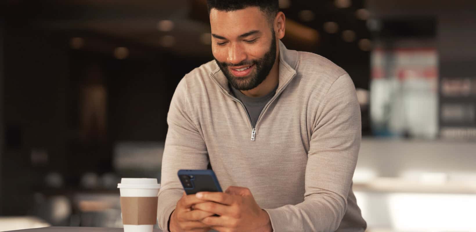 Man using a smartphone over coffee in a comfortable Nissan dealership waiting lounge.