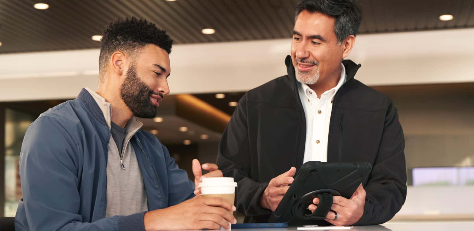 Nissan service advisor showing a tablet to a customer holding coffee in a service center.