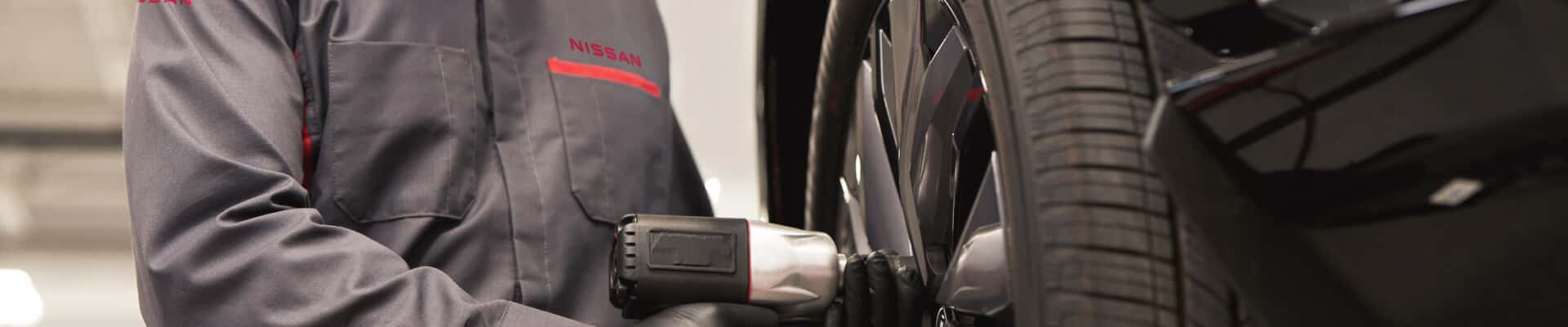 Nissan technician using an impact wrench on the wheel of a white vehicle in a service garage.
