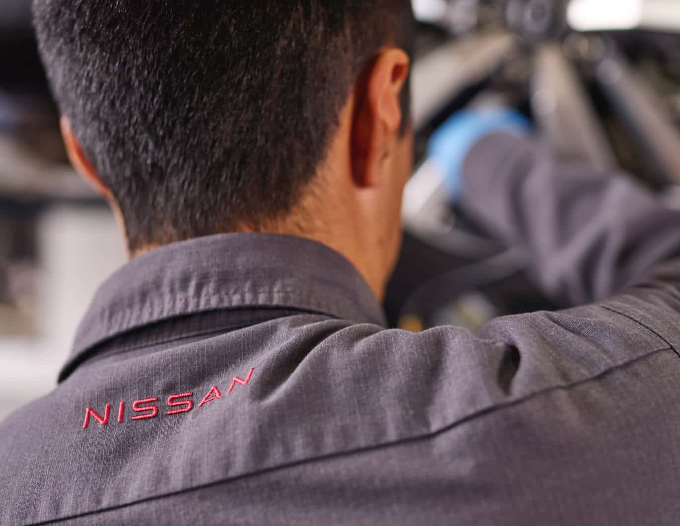 Close-up rear view of a technician wearing a grey shirt embroidered with the red Nissan logo.
