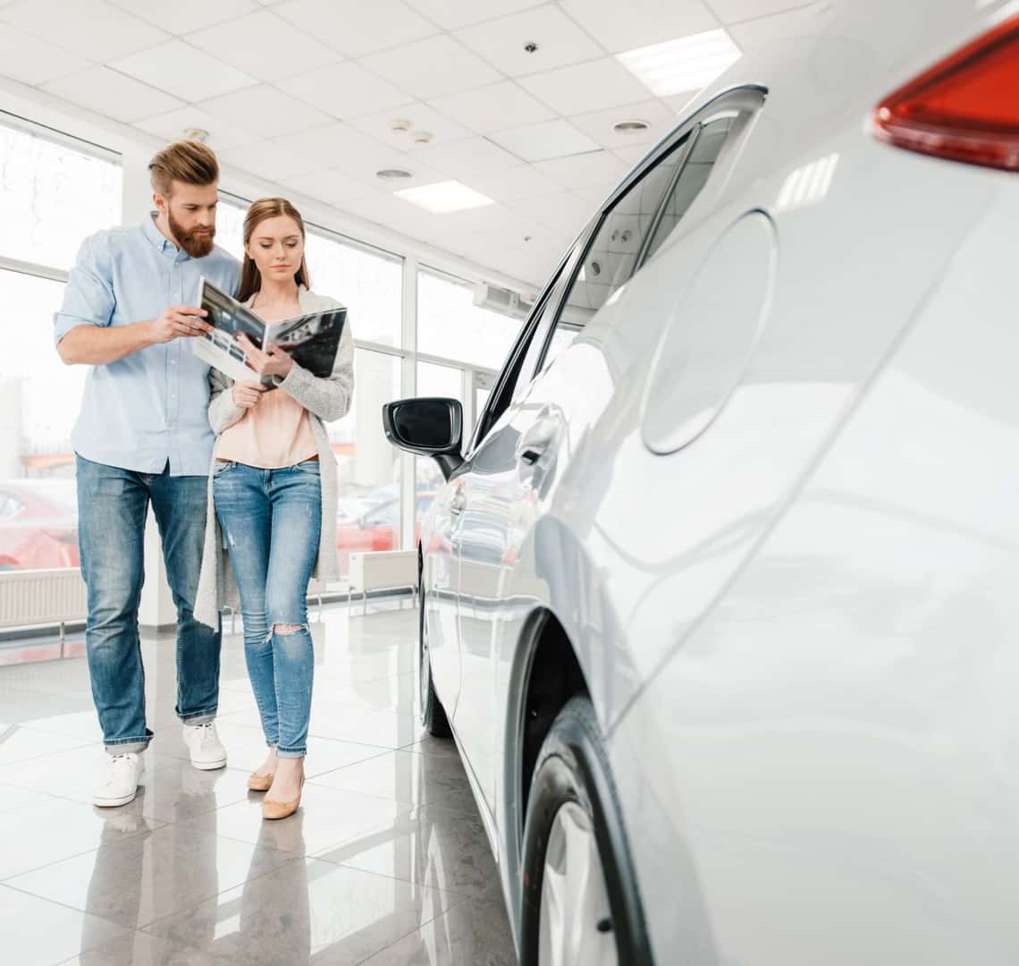 Couple reviewing vehicle information while browsing a car at a dealership.