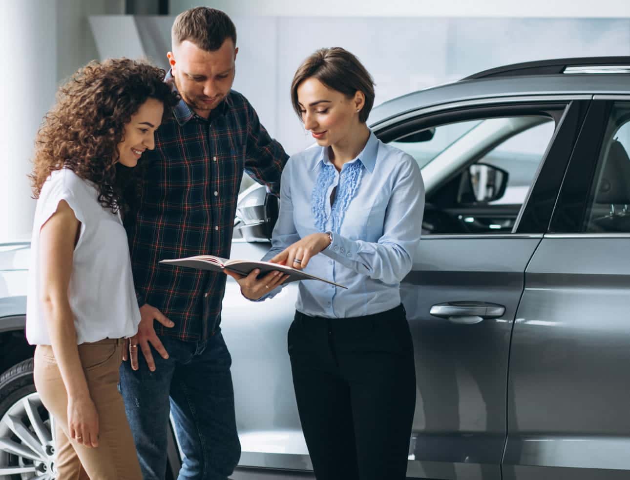 Sales representative reviewing information with a couple beside a gray SUV in a dealership showroom.