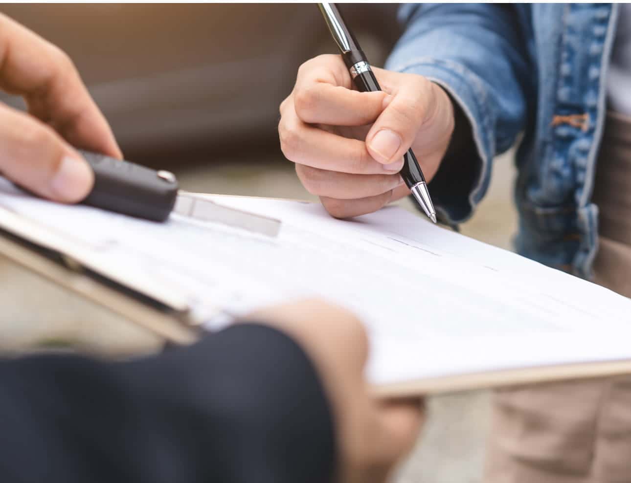 Close-up of a customer signing paperwork while another person holds a clipboard.