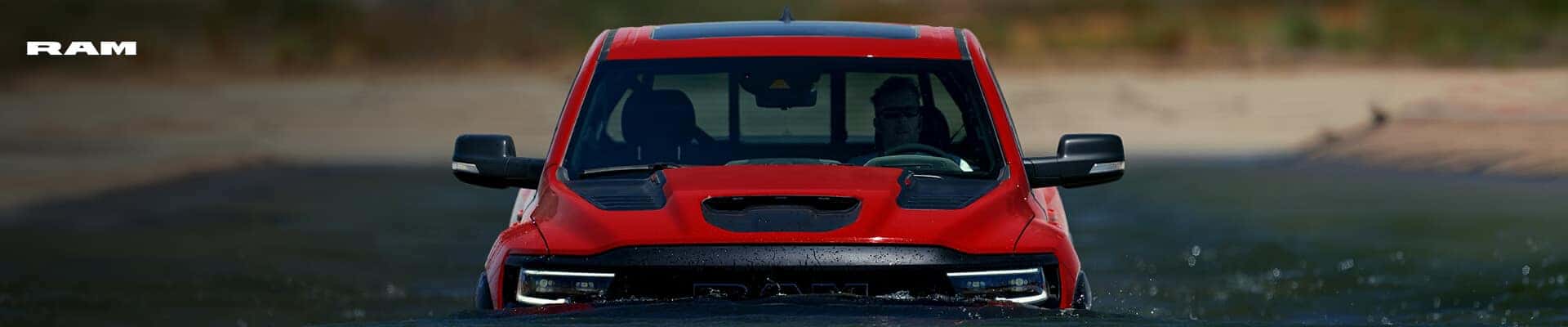 Front-view close-up of a Ram 1500 TRX in Red wading through deep river water.