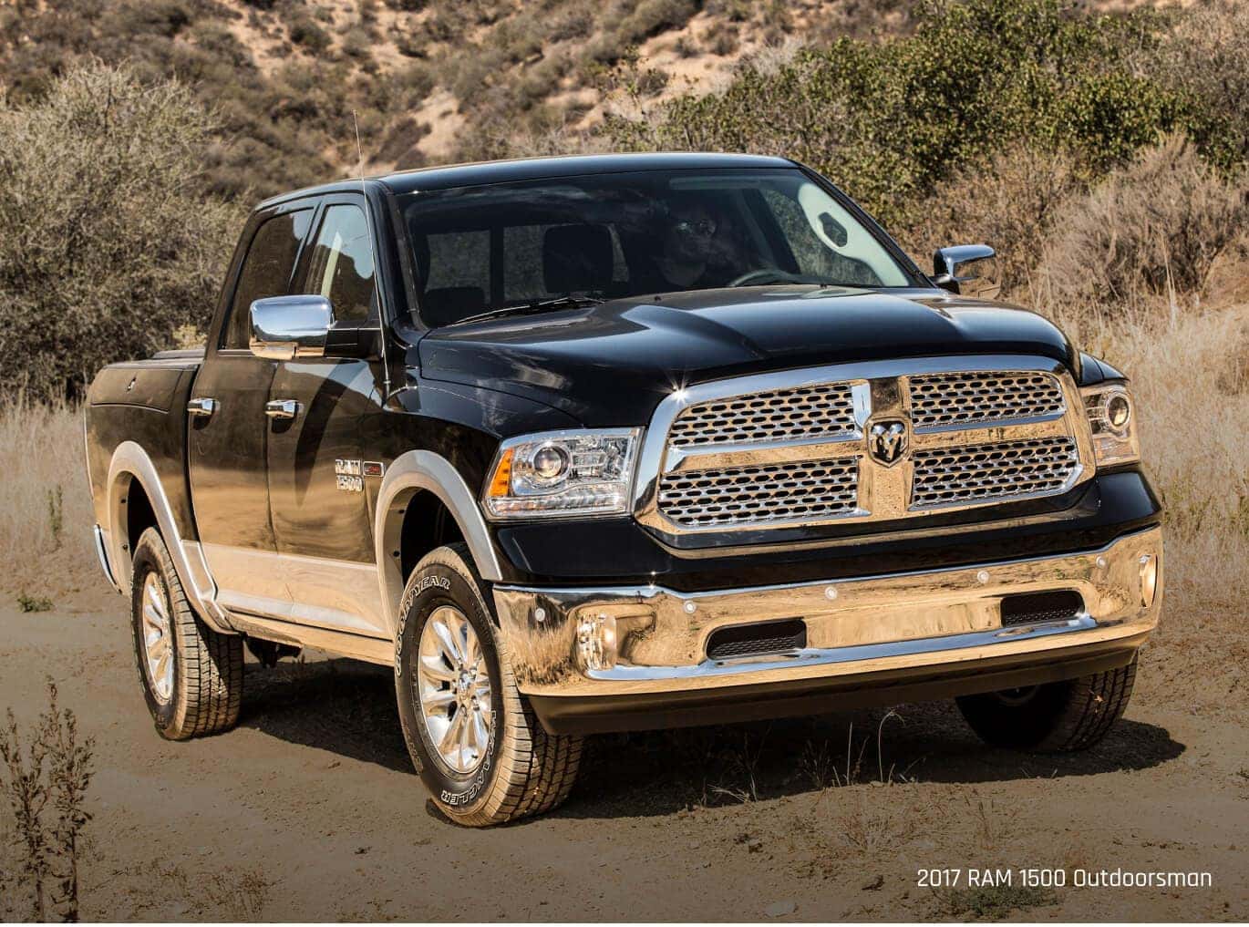 Three-quarter view of a Ram 1500 Outdoorsman in Black parked on a dirt path.