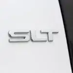 Close-up of the chrome SLT badge on a white GMC vehicle, highlighting the trim level designation.