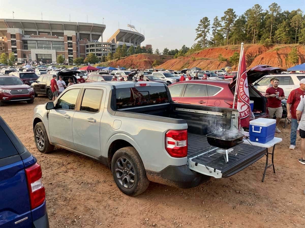 2026 Ford Maverick tailgate setup in a stadium parking lot with grill and cooler, game-day afternoon light