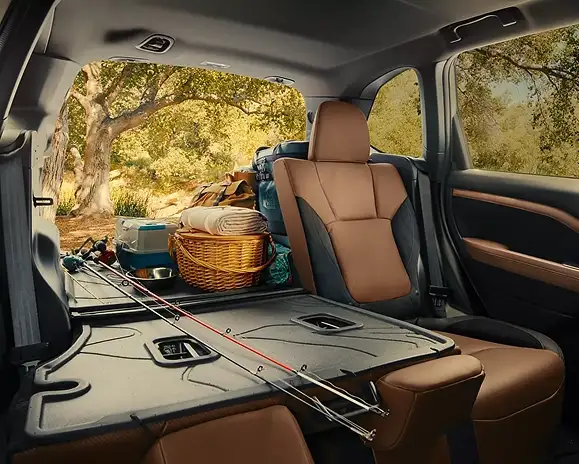 Rear cargo area of the 2026 Subaru Forester loaded with a picnic basket, cooler, and fishing rod, tailgate open to the woods