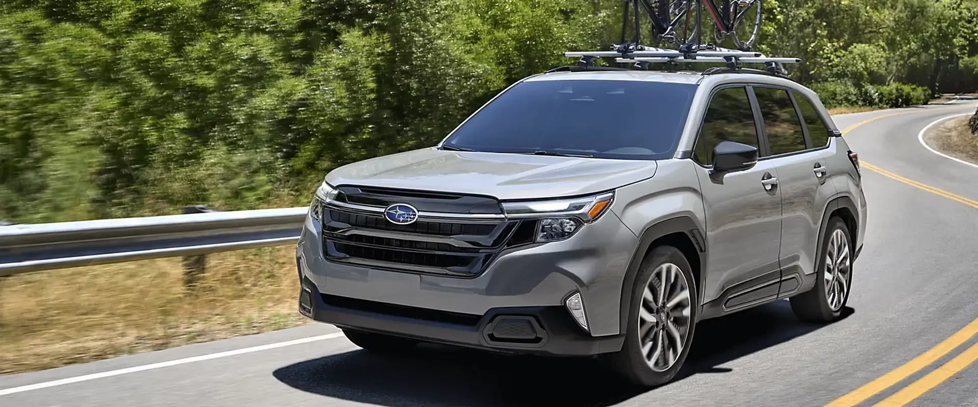 Silver 2026 Subaru Forester carrying two bikes on a roof rack along a winding mountain road