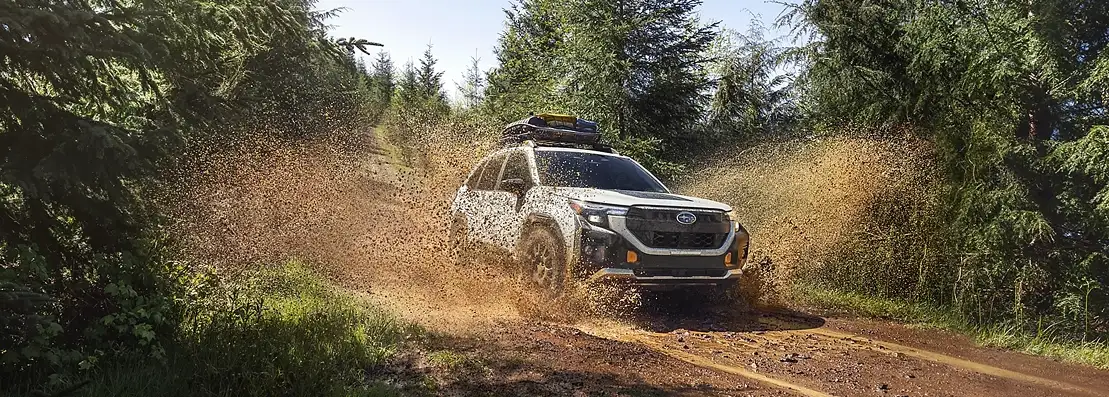 2026 Subaru Forester Wilderness splashing through mud on a forest trail