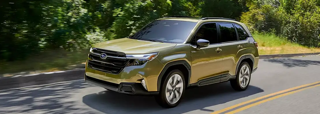 Green 2026 Subaru Forester driving on a tree-lined road