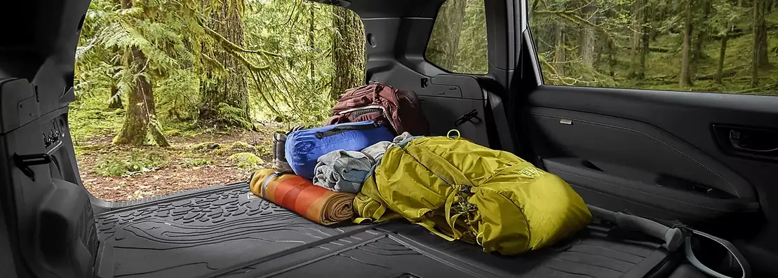 Rear cargo area of the 2026 Subaru Forester loaded with camping gear, tailgate open to a misty forest
