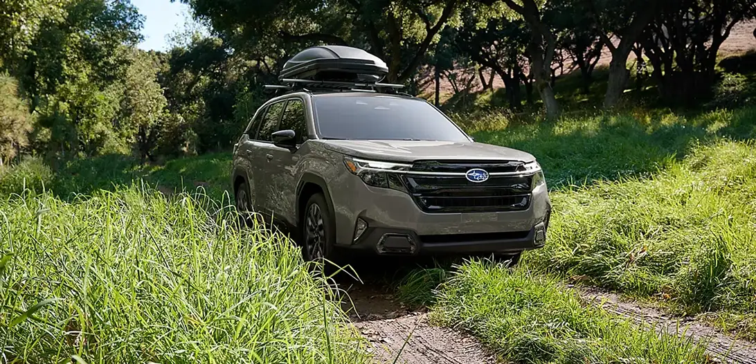Green 2026 Subaru Forester with a roof cargo box parked on a grassy off-road trail