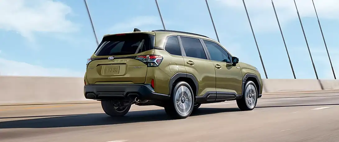 Rear view of a green 2026 Subaru Forester driving across a bridge