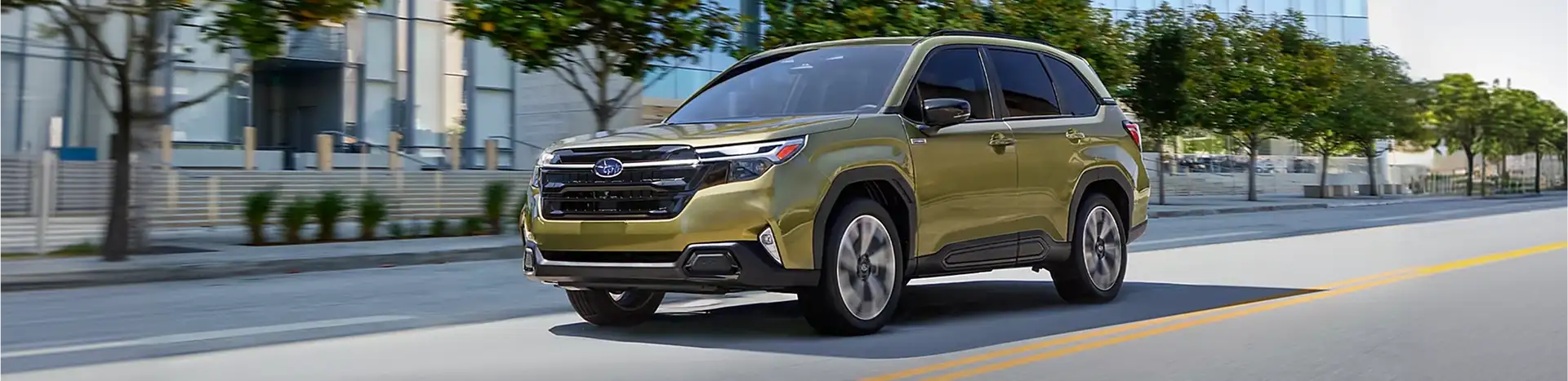Green 2026 Subaru Forester driving on a city street past modern glass buildings