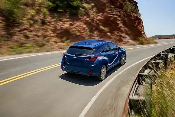 Rear view of a blue 2026 Subaru Impreza driving on a canyon road