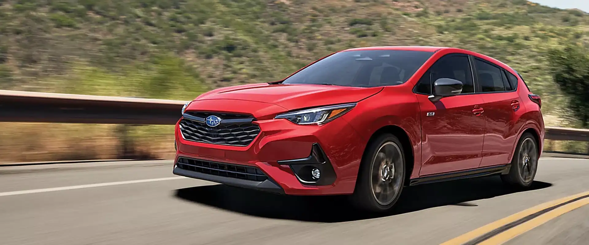 Red 2026 Subaru Impreza hatchback driving on a winding mountain road