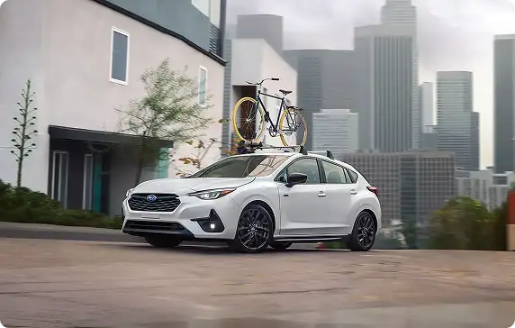 White 2026 Subaru Impreza with a bike on a roof rack and a city skyline behind