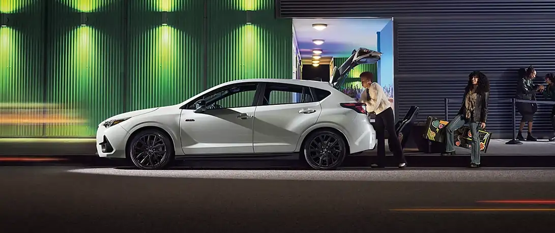 White 2026 Subaru Impreza parked at night while people load gear outside a lit building