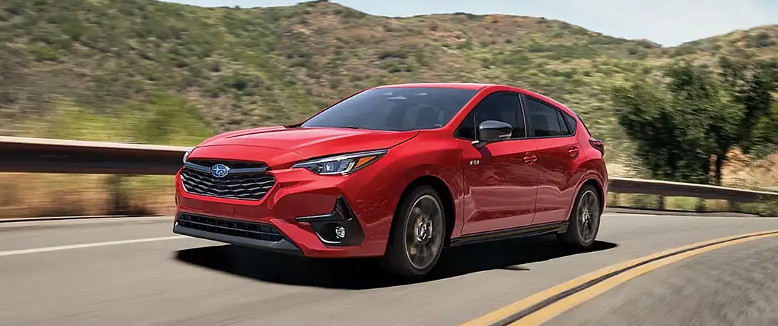 Red 2026 Subaru Impreza driving on a scenic mountain road