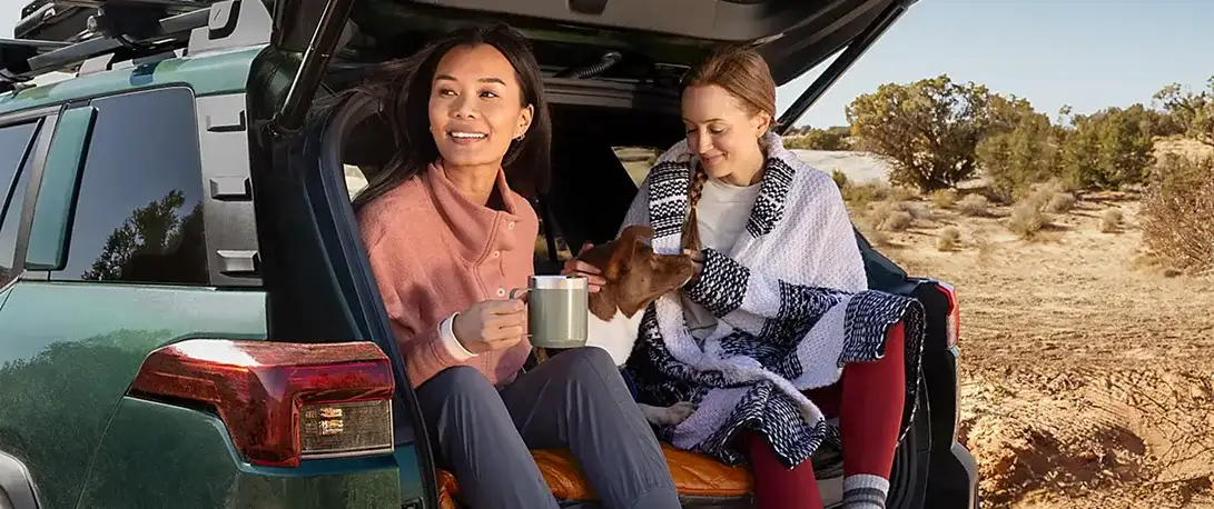 Two people relaxing at the open rear gate of a 2026 Subaru Outback