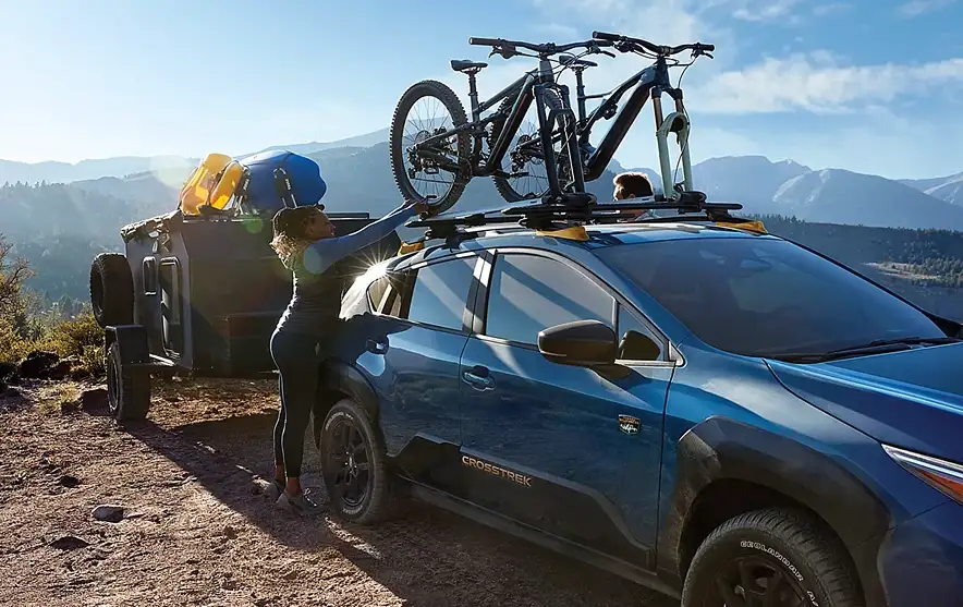Woman loading mountain bikes and gear onto a blue Subaru Crosstrek at a mountain overlook