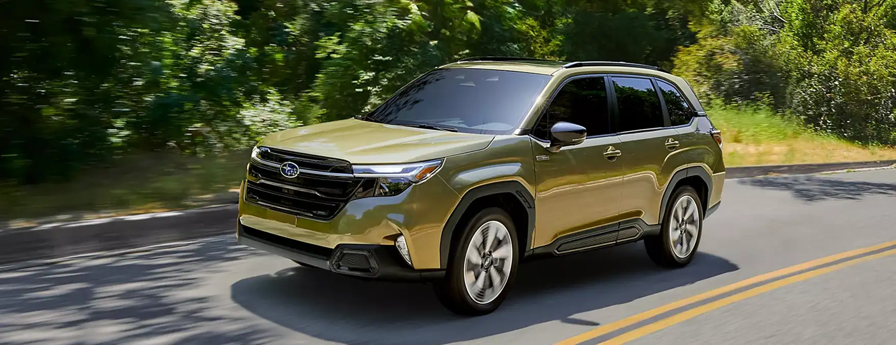 Gold 2025 Subaru Forester driving on a tree-lined mountain road