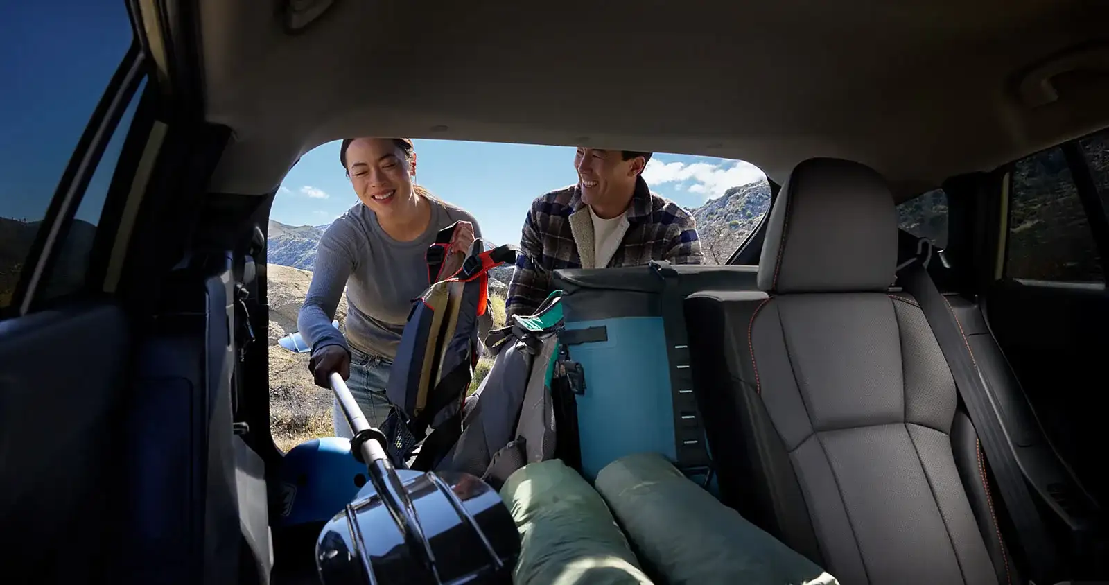 Two owners loading camping gear into the open cargo area of a 2026 Subaru Crosstrek at a mountain overlook, the recreation use that keeps a Las Vegas Subaru on the shorter service cadence