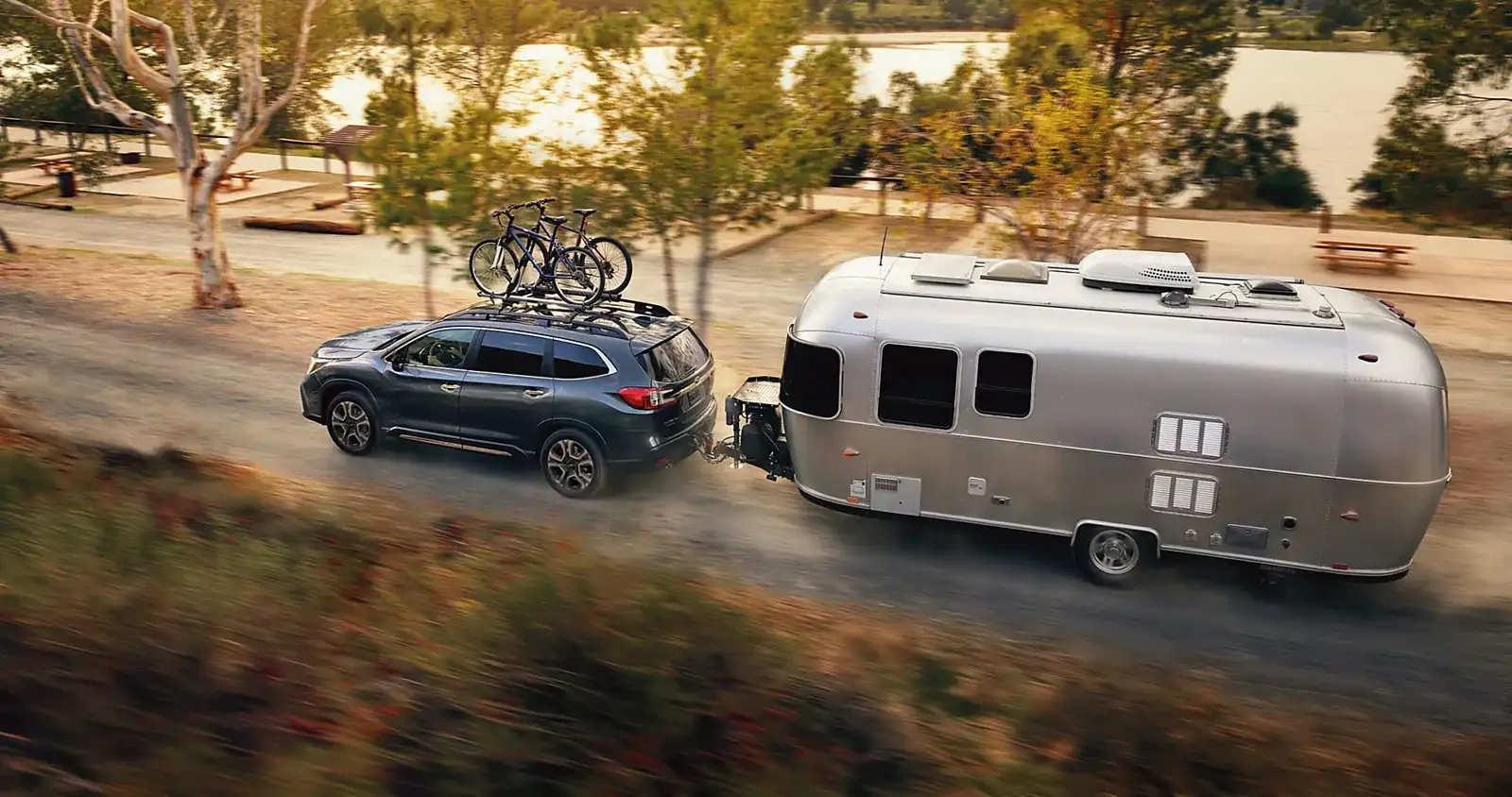 A 2026 Subaru Ascent with bikes on the roof towing an Airstream trailer along a dusty lakeside trail, the towing and dust duty cycle that puts a Las Vegas Subaru on the severe-duty schedule