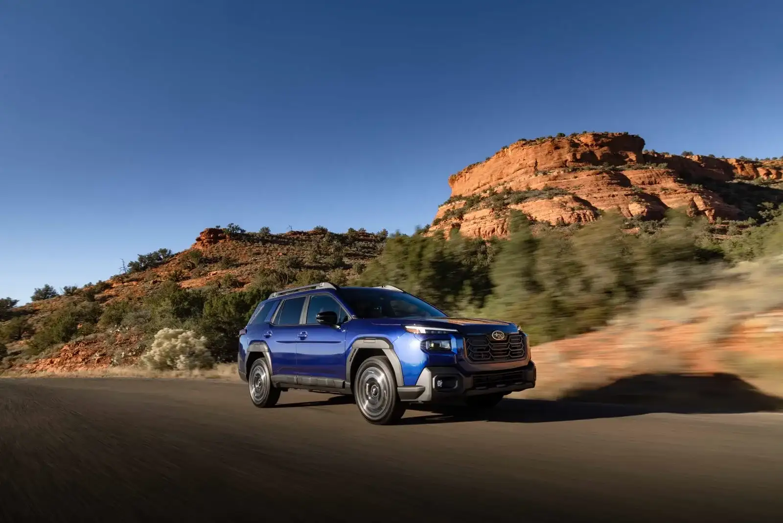A blue 2026 Subaru Outback in motion on a red-rock desert road, the AWD crossover Las Vegas buyers pick for clearance and park trips