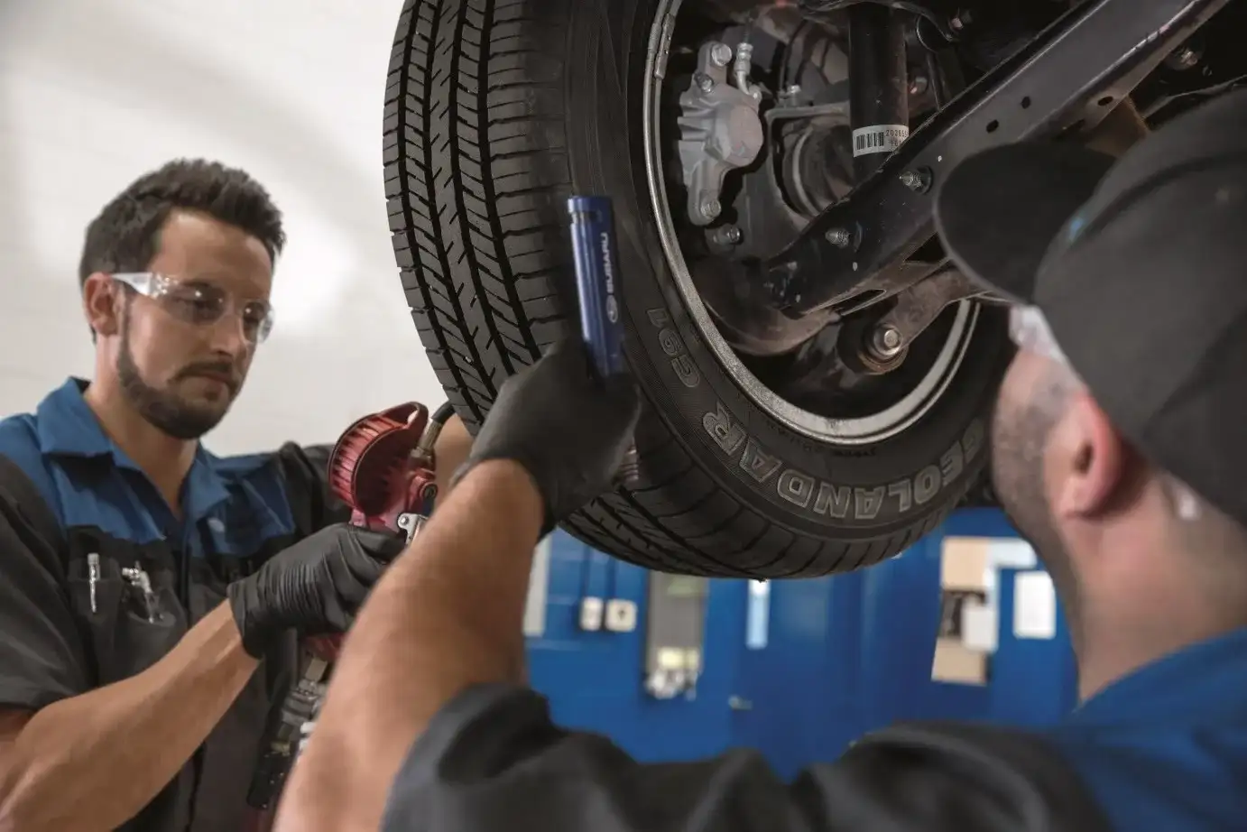 Two Subaru-trained technicians inspecting the tire and brake assembly on a lifted Subaru during a multi-point inspection
