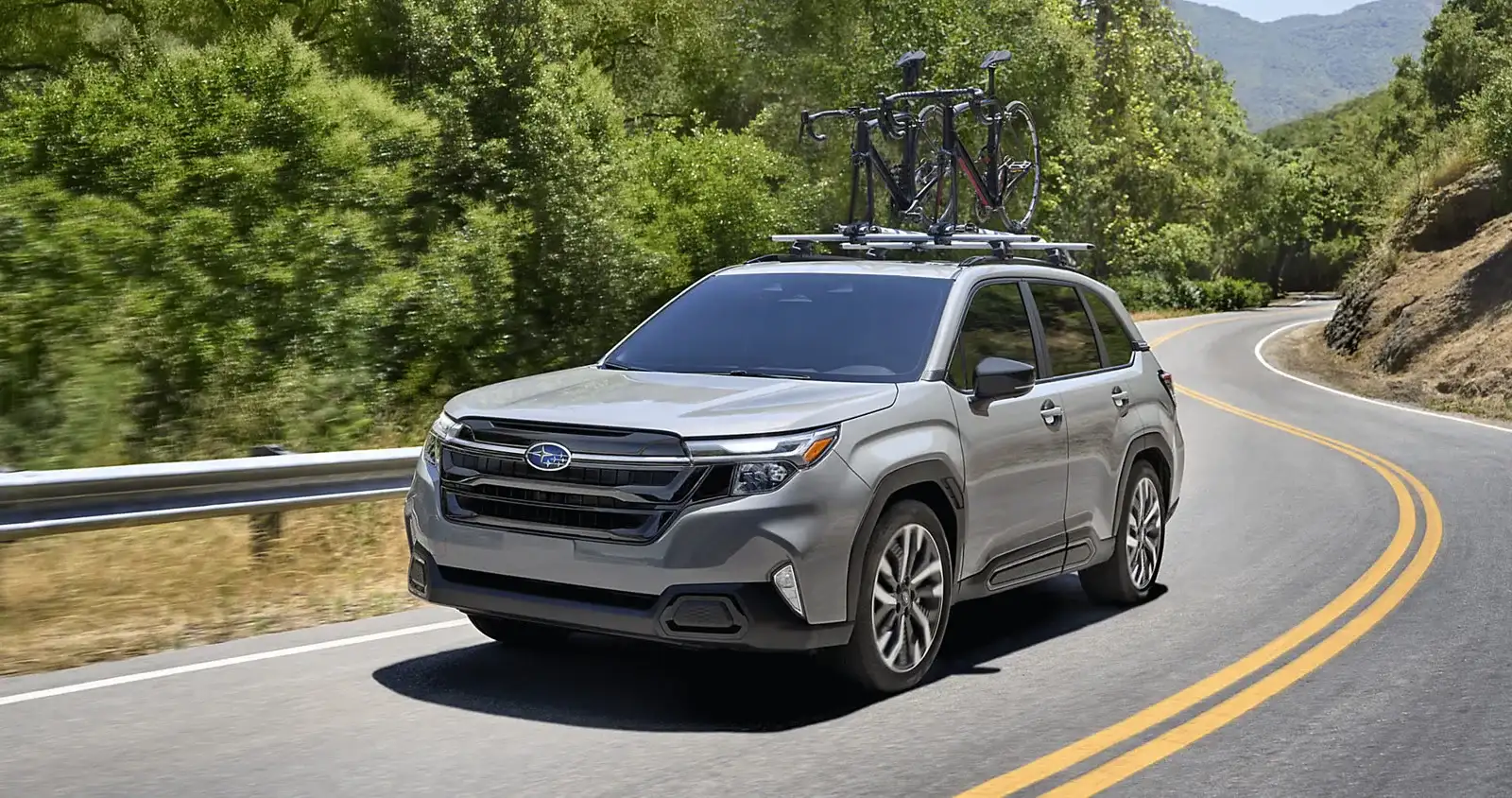 A 2026 Subaru Forester carrying bikes on the roof, cornering on a mountain highway with standard Symmetrical AWD