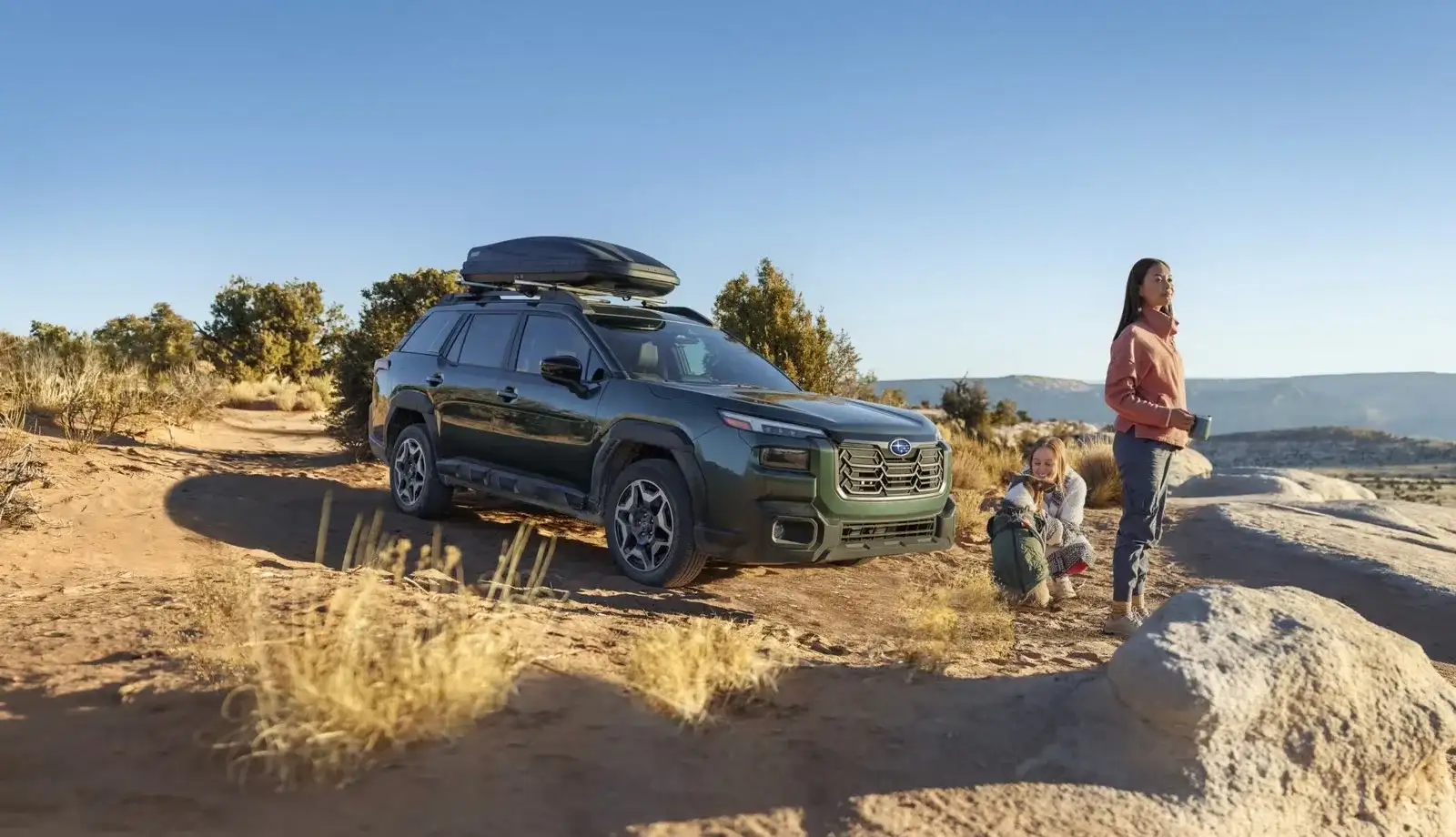 A 2026 Subaru Outback Wilderness parked at a red-rock desert overlook with a family beside it, gear loaded on the roof