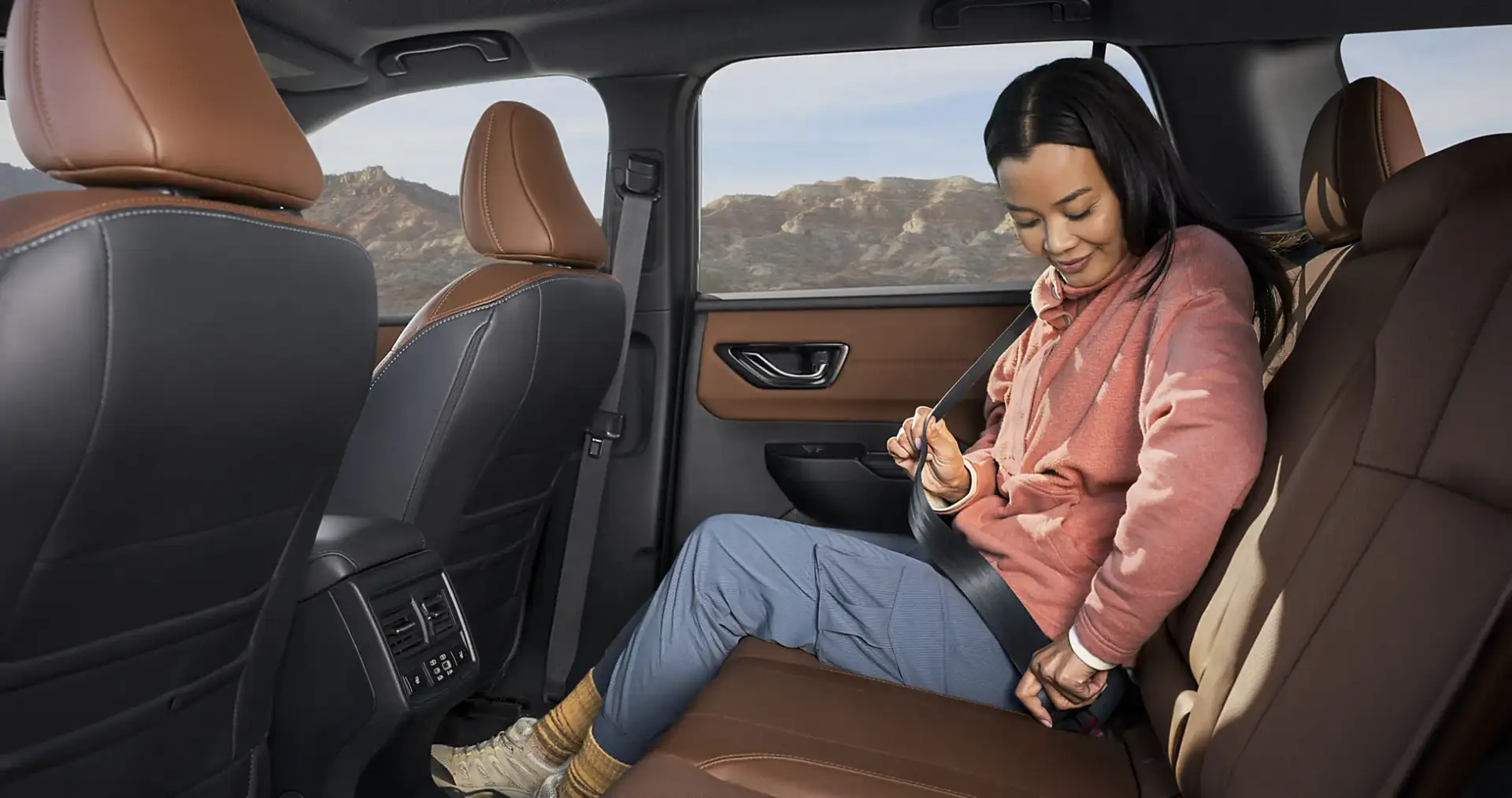 A passenger buckling in the spacious rear seat of a 2026 Subaru Outback, with desert mountains visible through the side window