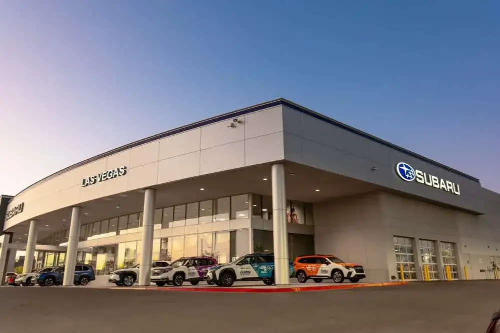 The Findlay Subaru of Las Vegas dealership building at dusk, with the Subaru sign lit and Love Promise community vehicles parked under the entrance canopy at 6455 Roy Horn Way.