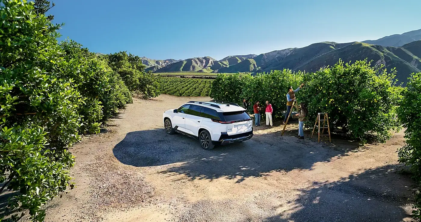 The 2027 Subaru Getaway parked in an orchard as a family gathers fruit, mountains beyond.