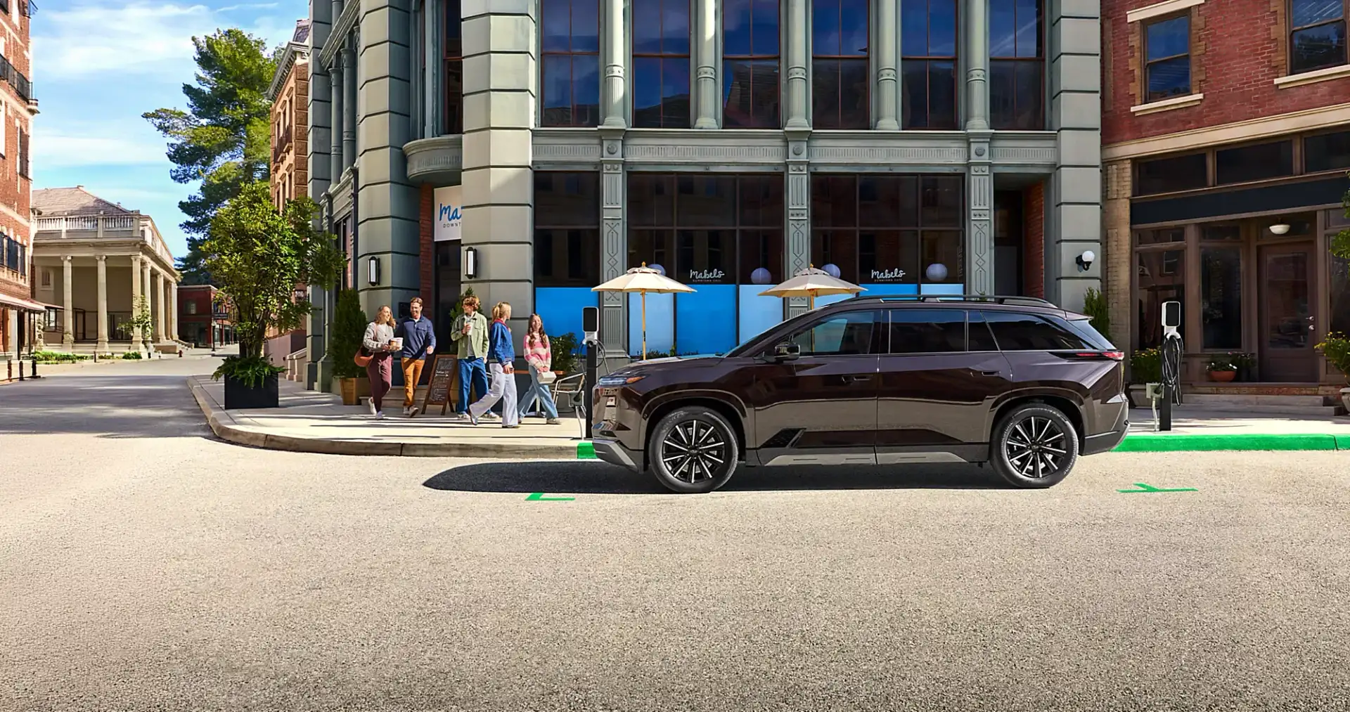 Side profile of the 2027 Subaru Getaway parked on a downtown street beside an EV charger.