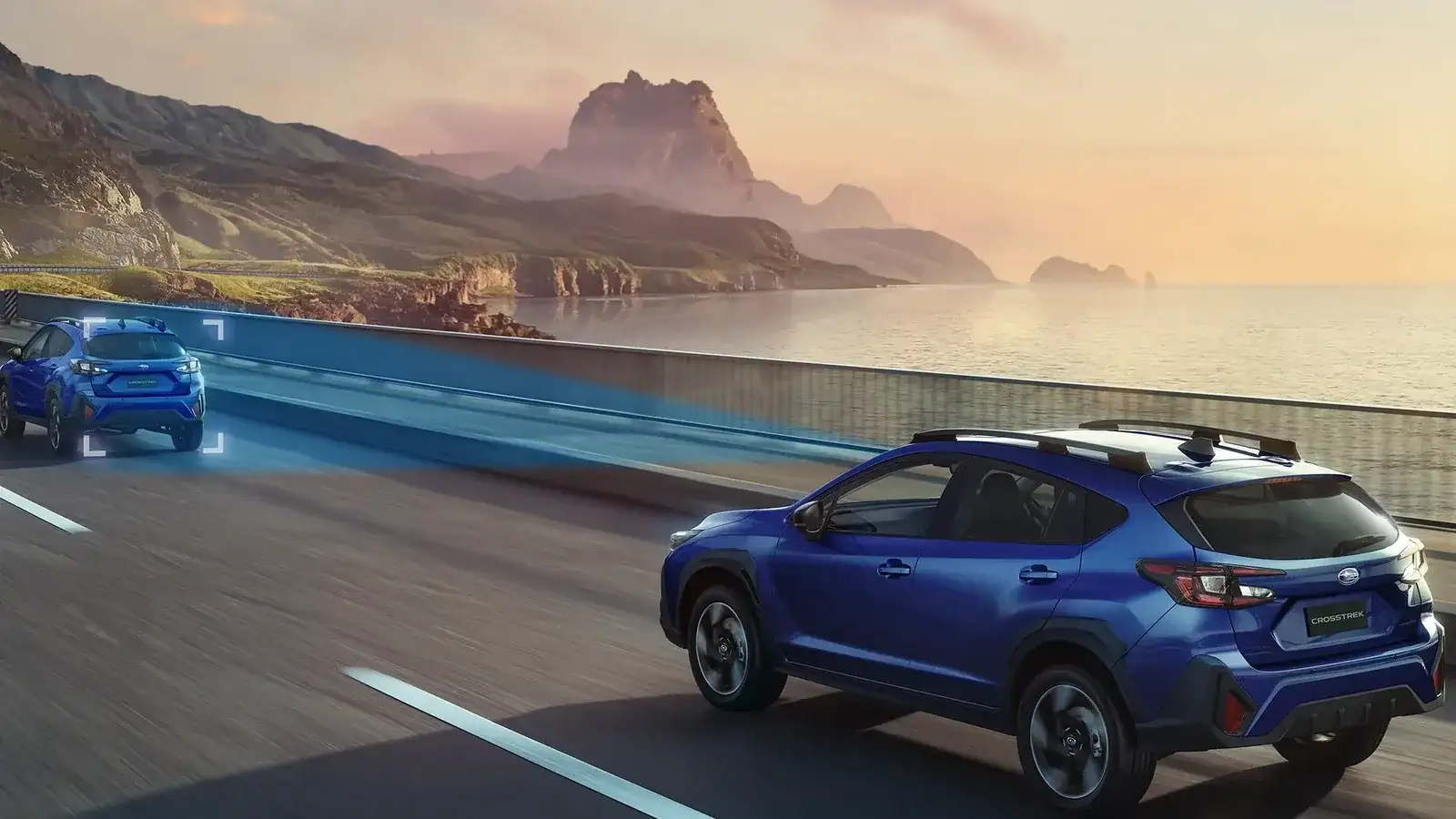 A blue 2026 Subaru Crosstrek on a scenic coastal highway at sunset, with a second Crosstrek following behind