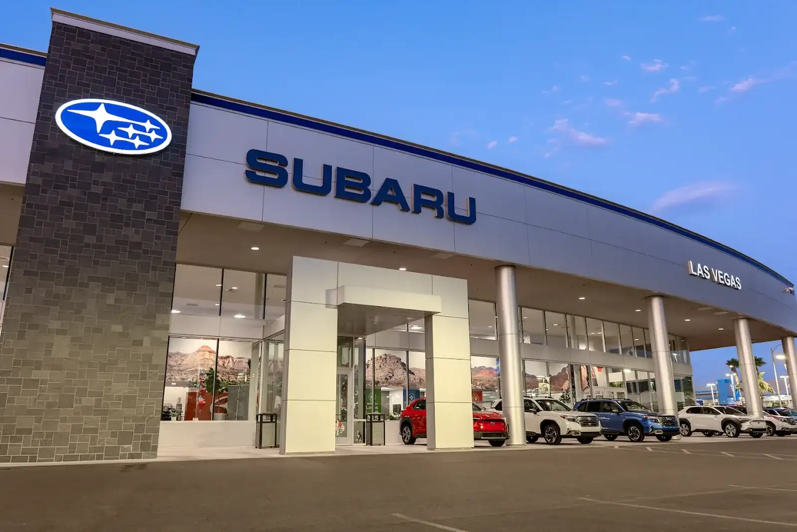 The Findlay Subaru of Las Vegas dealership at dusk, showroom lit and new Subarus out front at 6455 Roy Horn Way
