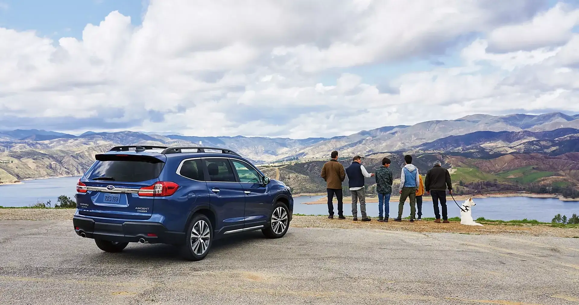 A Subaru Ascent parked at a mountain-lake overlook while a family takes in the view, the kind of weekend a three-row Subaru SUV is built for