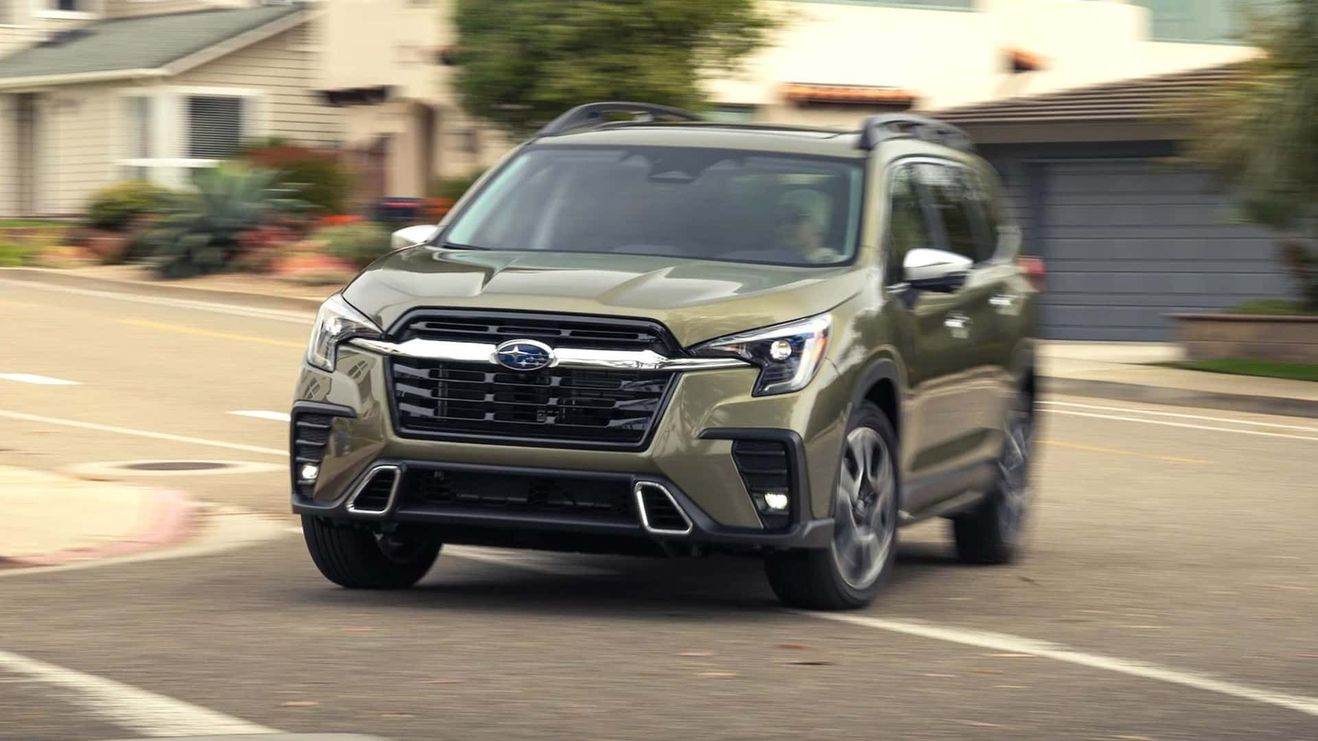 A 2026 Subaru Ascent in olive green driving through a suburban neighborhood, front three-quarter view
