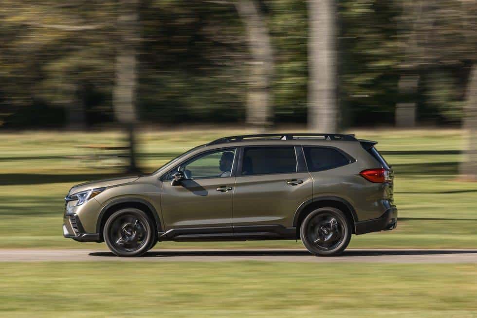 A 2026 Subaru Ascent in olive green driving past a tree-lined park, side profile