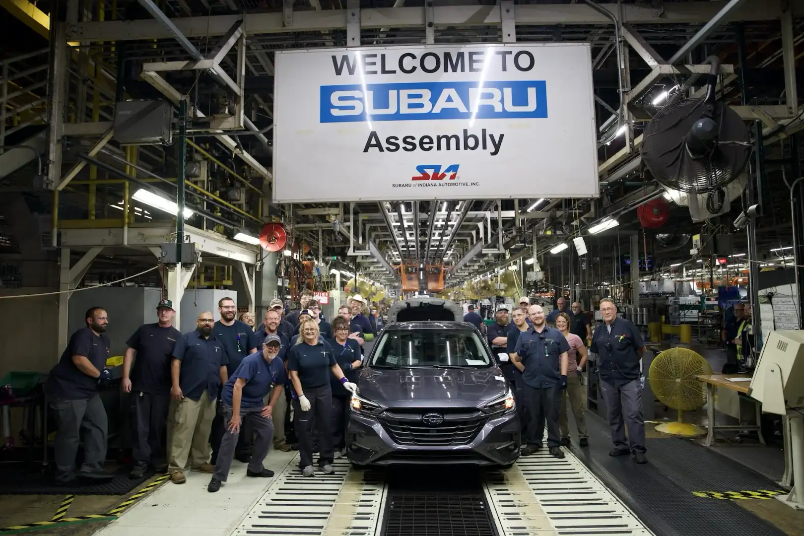 Subaru of Indiana Automotive Assembly line workers around a Grey Subaru Legacy