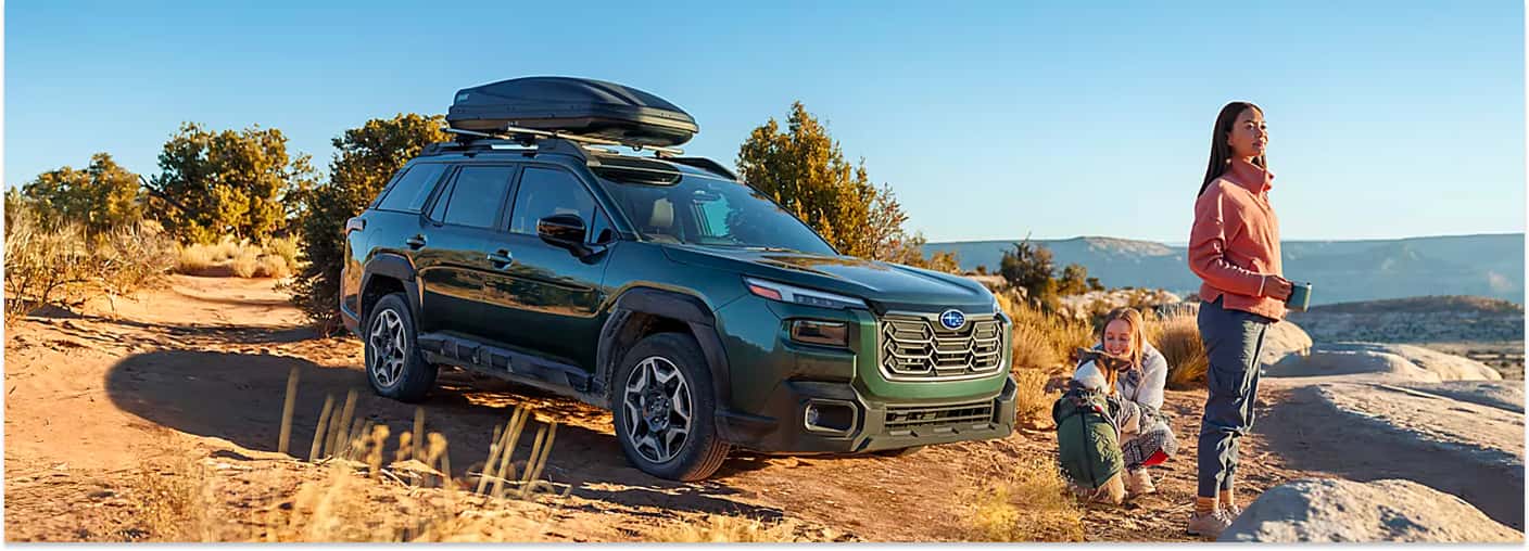 Dark green 2026 Subaru Outback with a roof cargo carrier parked on a desert trail.