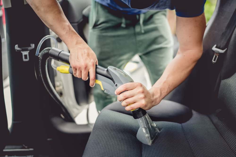 Detailer showing how to vacuum and clean vomit from a fabric car seat