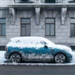 Blue car covered in snow parked in front of a stone building